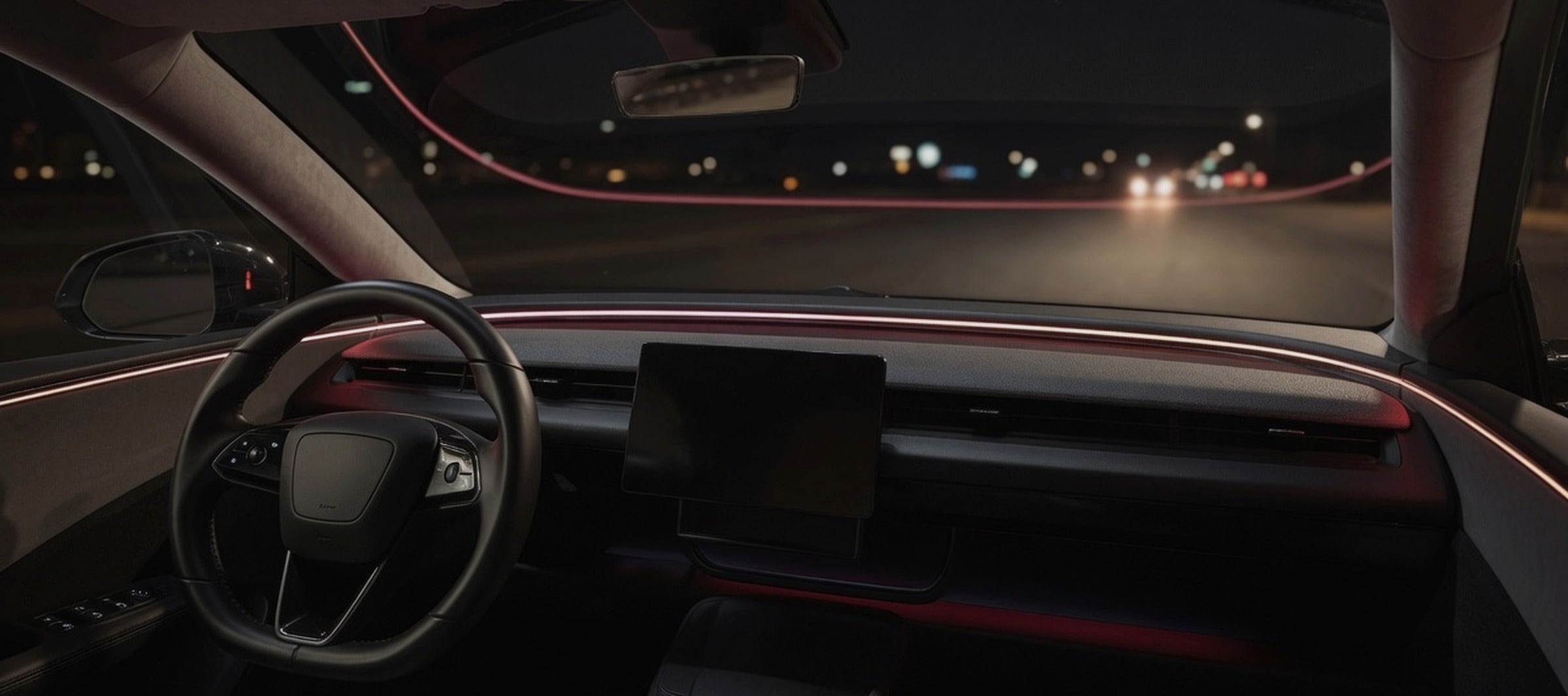 Car dashboard at night with red ambient lighting and the road ahead