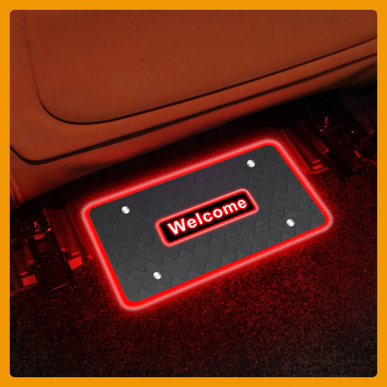Illuminated red 'Welcome' LED floor mat light glowing in the footwell of a car with tan leather seats at night