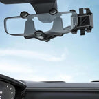 Rearview mirror phone holder clamped onto a car's rear-view mirror, seen from the driver's seat with the dashboard below