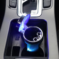 The LED ashtray sitting in a car centre console cup holder with the lid open and the light ring lit