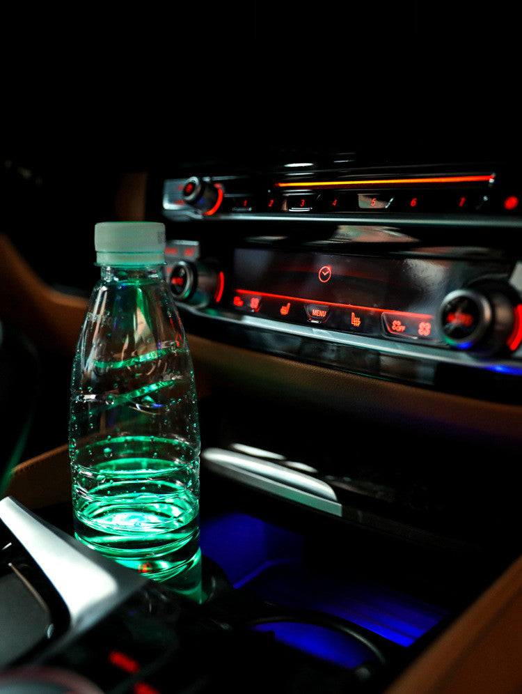 Coaster glowing green under a water bottle in a car cup holder beside a red-lit centre console at night