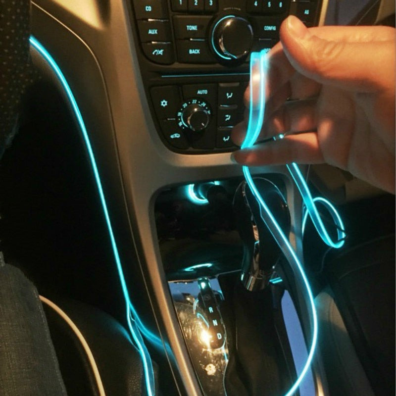 Hand tucking a glowing ice-blue EL neon strip into the trim seam beside a car's centre console