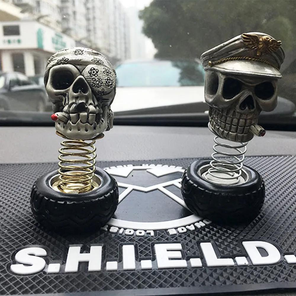 Two spring-mounted skull ornaments on a car dashboard mat with the windshield view behind