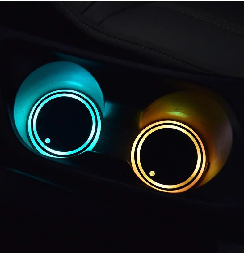 Two LED cup holder coasters glowing cyan and amber in a car centre console at night
