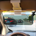 Anti-glare car sun visor flipped down behind the windscreen, cutting glare on a city street, seen from the driver's seat