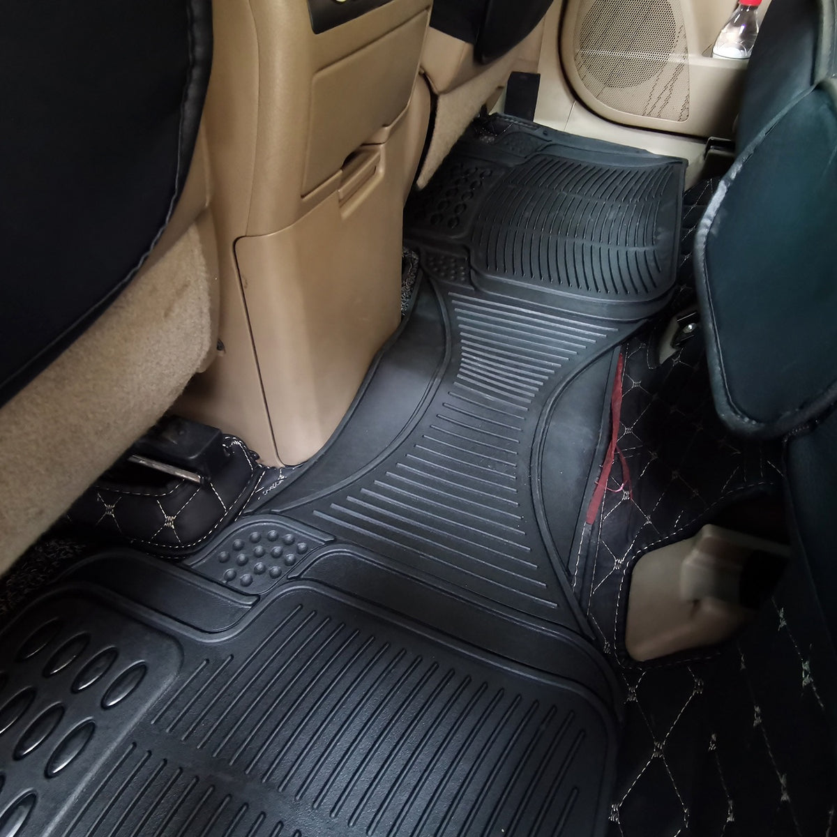 Rear rubber floor mat installed across the back footwell of a car, seats and centre console visible