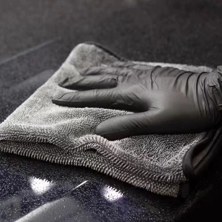 Gloved hand drying dark car paintwork with the microfiber towel