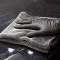Gloved hand drying dark car paintwork with the microfiber towel