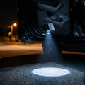 Wireless car door projector lights, 2 pack, projecting onto the ground beside an open car door